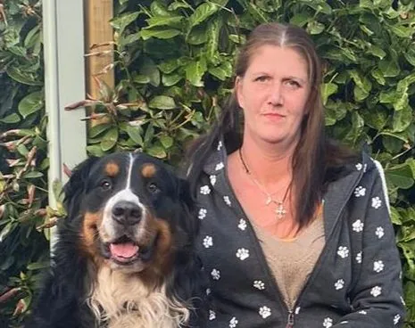 Sabrina Stüber sitzt mit einem Berner Sennenhund vor einer grünen Hecke